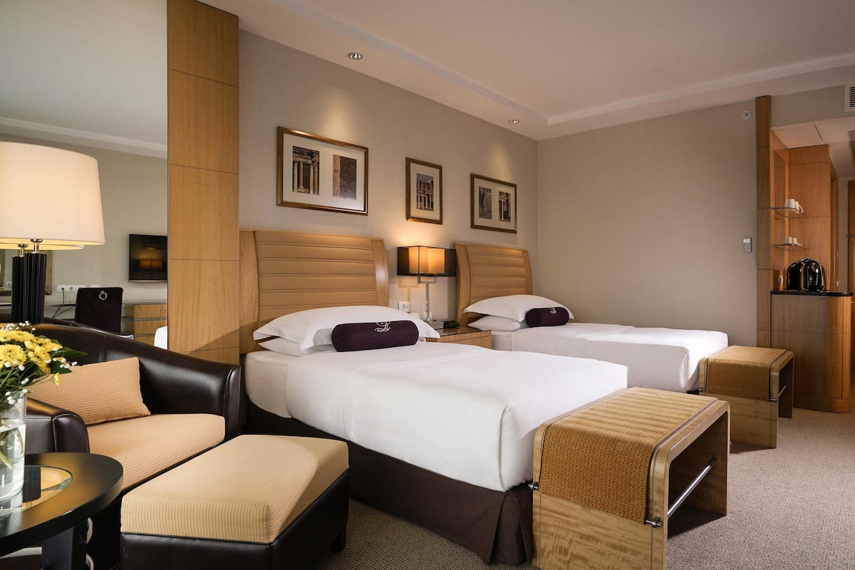 A hotel room with two beds, a sofa, a small table with a vase, and a cabinet.
