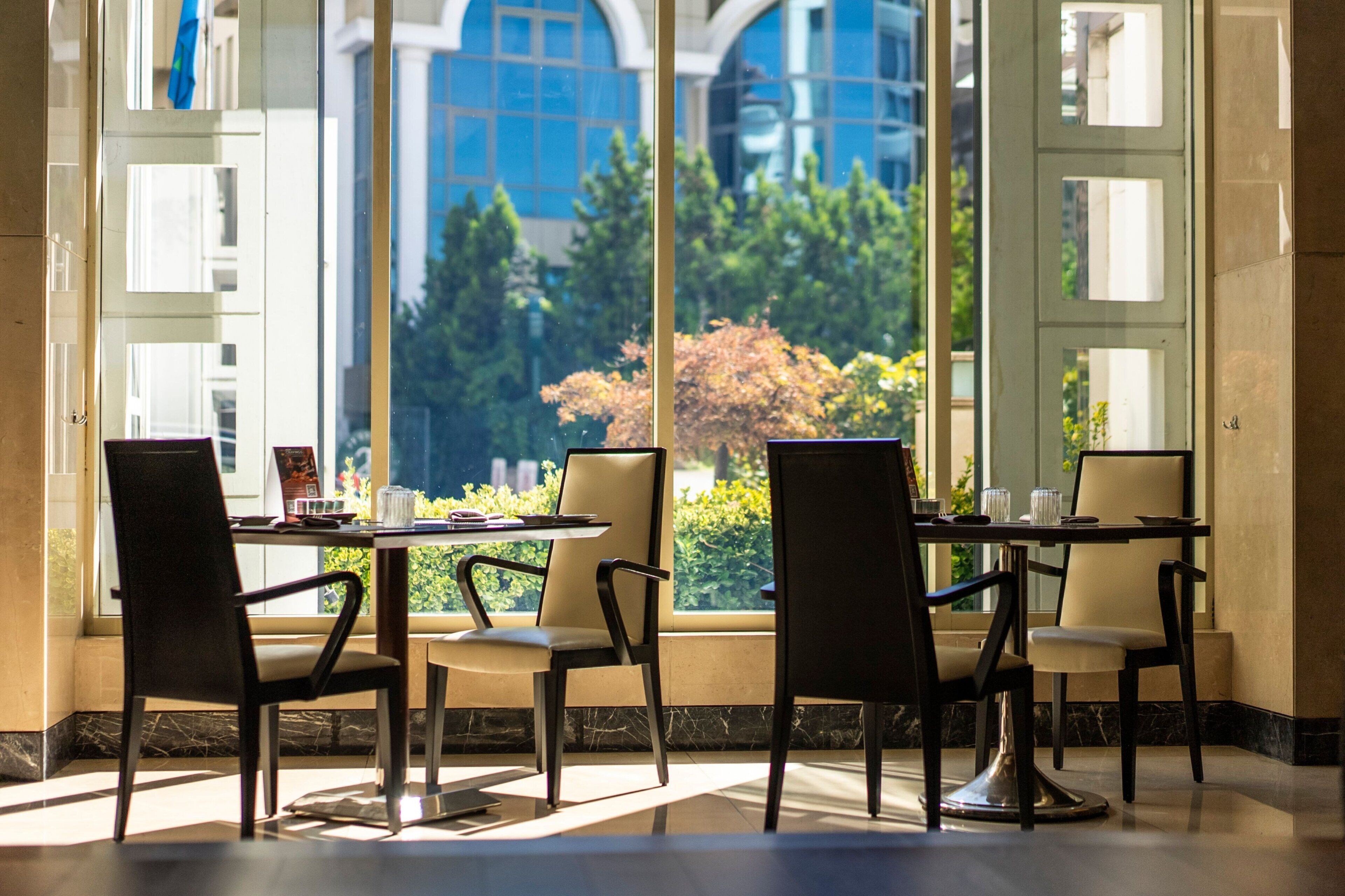 A dining area with a table and chairs, large windows with a view of greenery and buildings, and a modern interior design.
