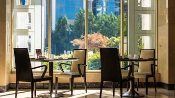 A dining area with a table and chairs, large windows with a view of greenery and buildings, and a modern interior design.