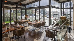 A restaurant with large windows, wooden tables, and wicker chairs.