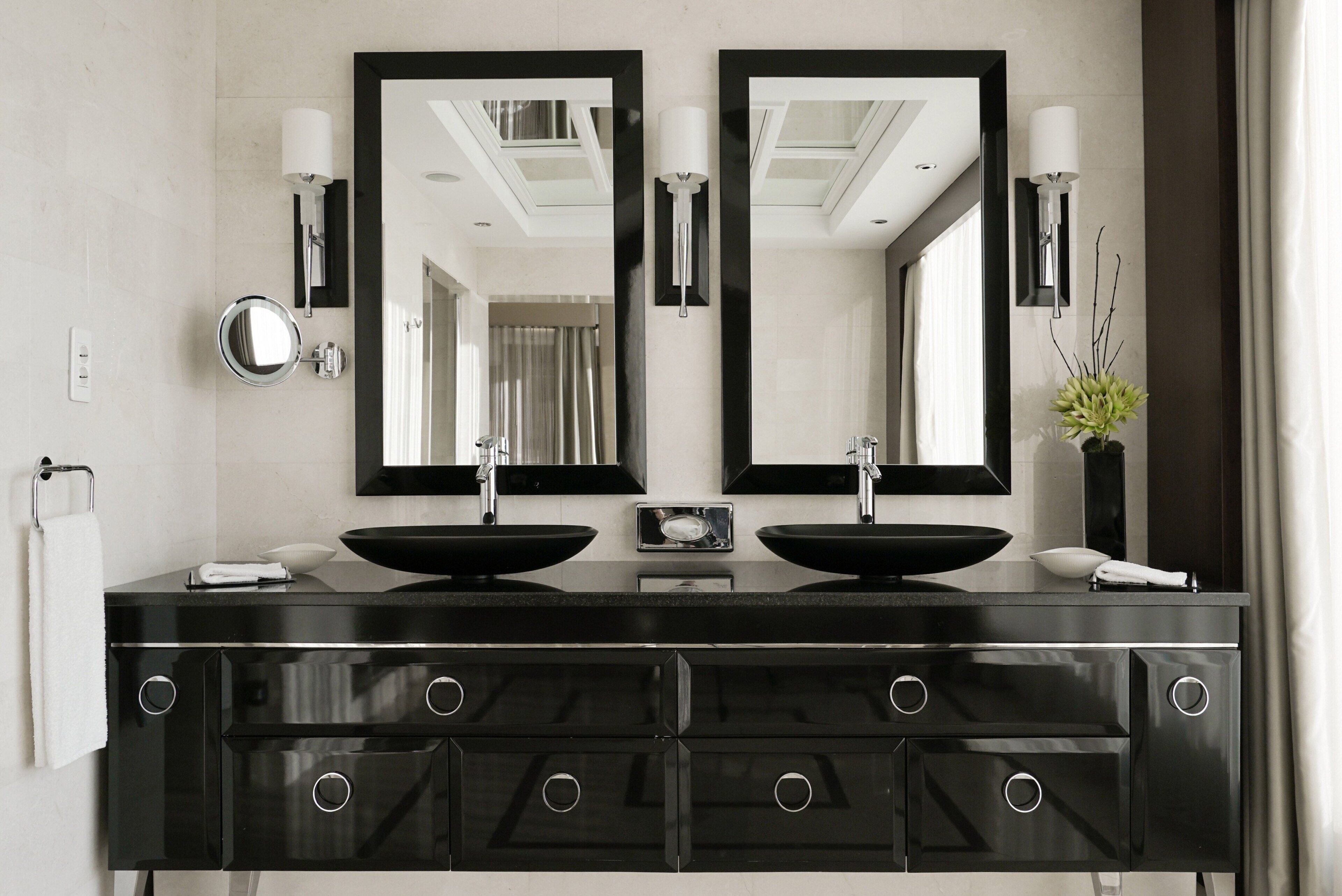 A modern bathroom with two black sinks, a large mirror, and a black vanity with multiple drawers.