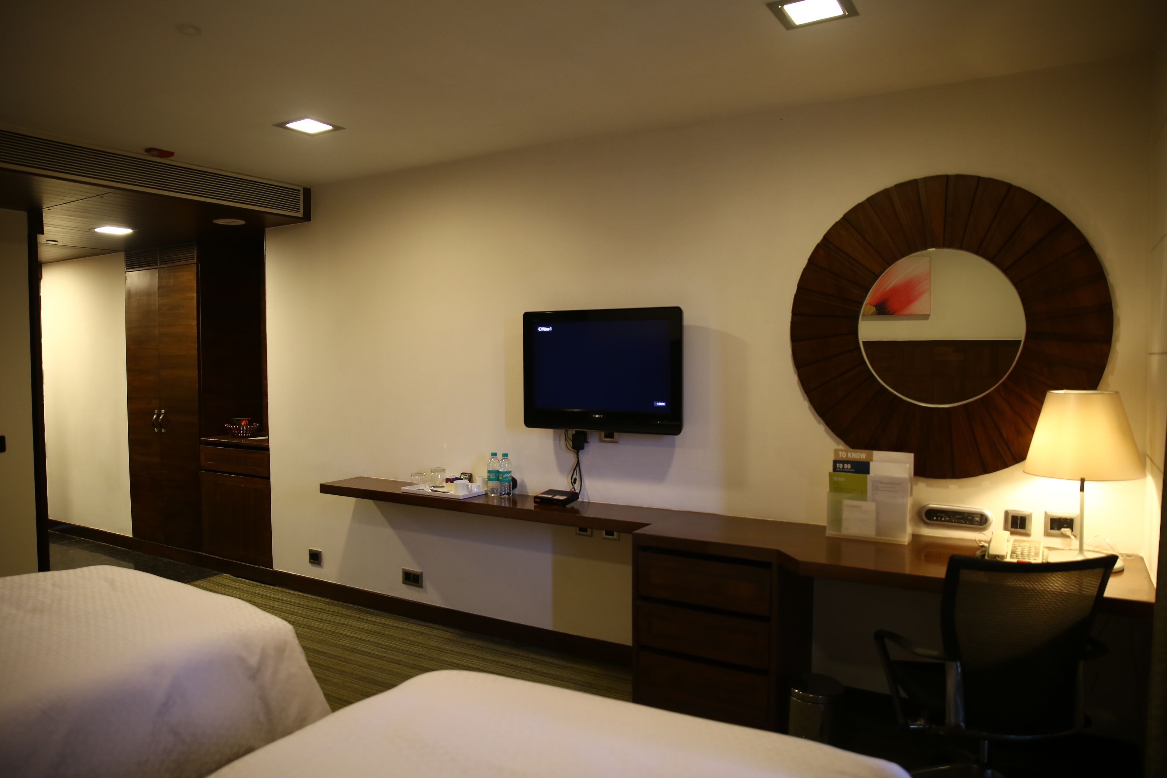A hotel room with two beds, a desk with a television, a mirror, a lamp, and a chair.