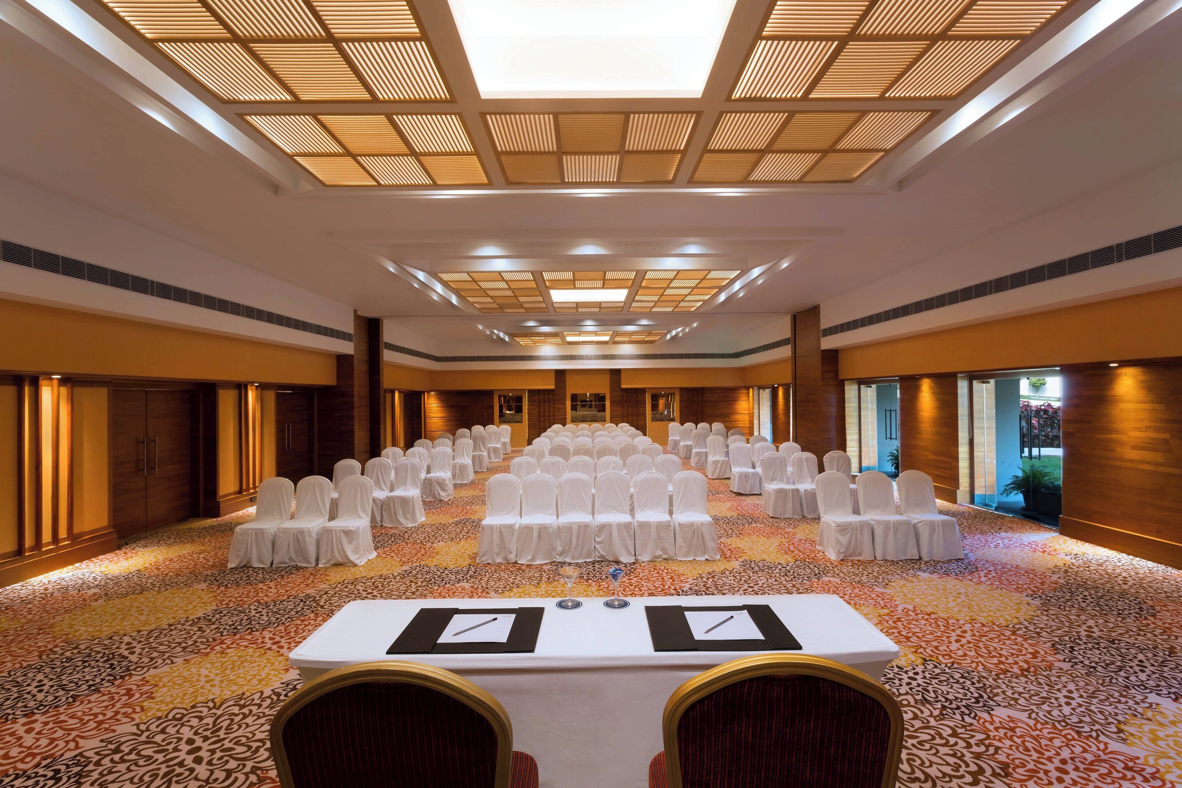 A conference room with rows of white chairs, a long table with nameplates, and a patterned carpet.