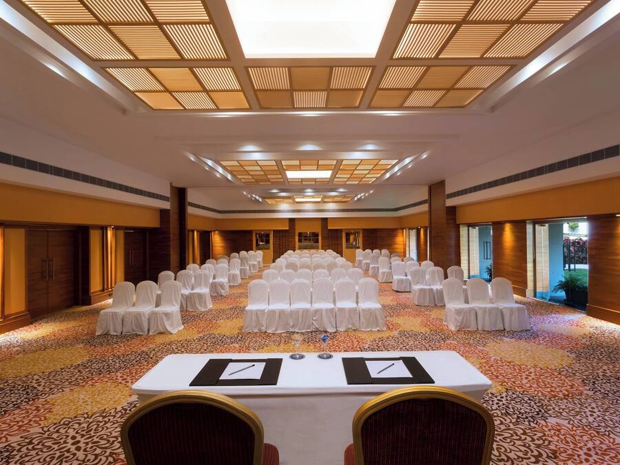 Un salón de conferencias con filas de sillas blancas, una mesa grande con tarjetas de identificación y una alfombra estampada.