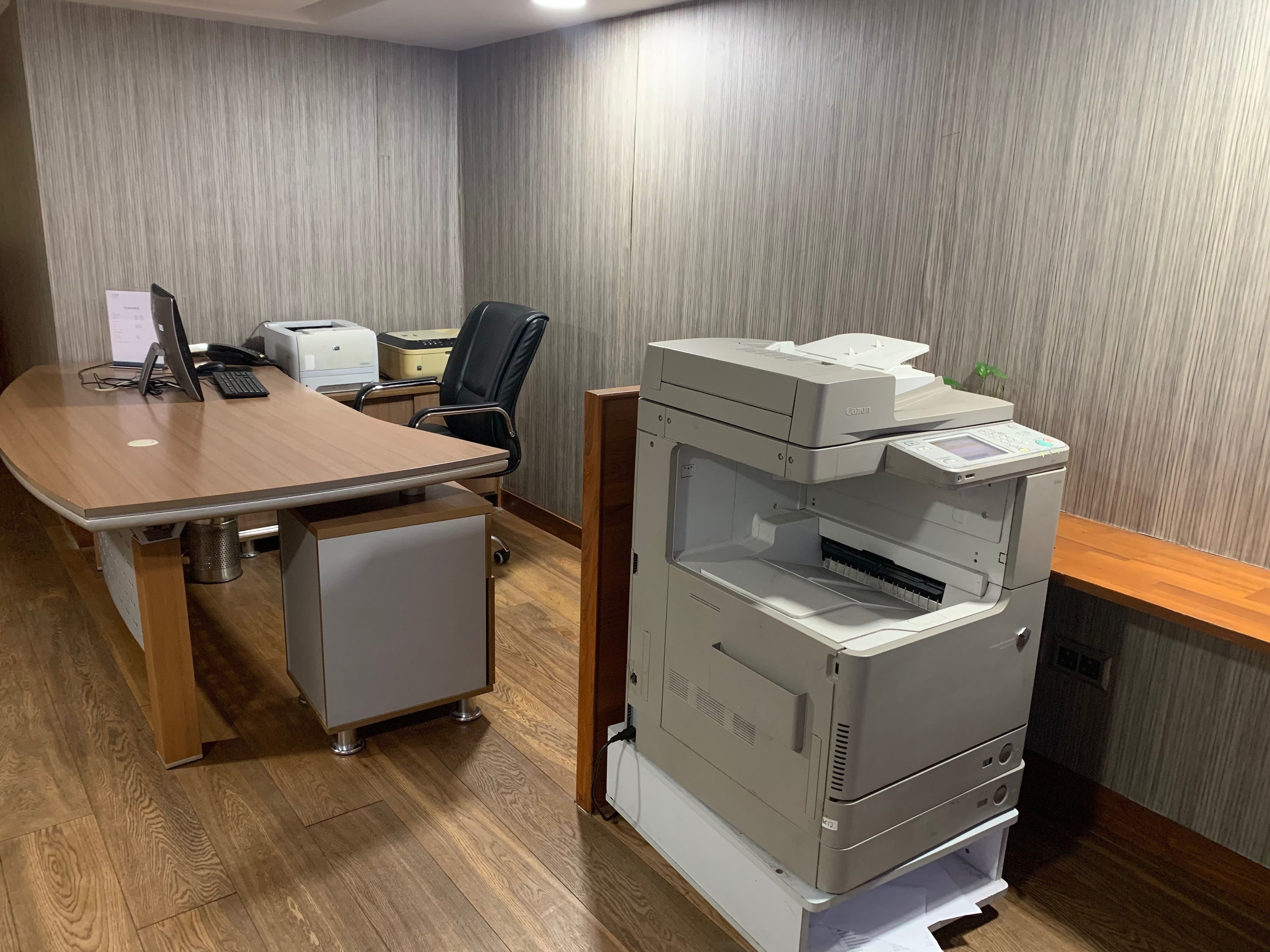 Una sala de conferencias con una mesa de madera, una silla de oficina negra, un ordenador de escritorio, una impresora y un archivador.