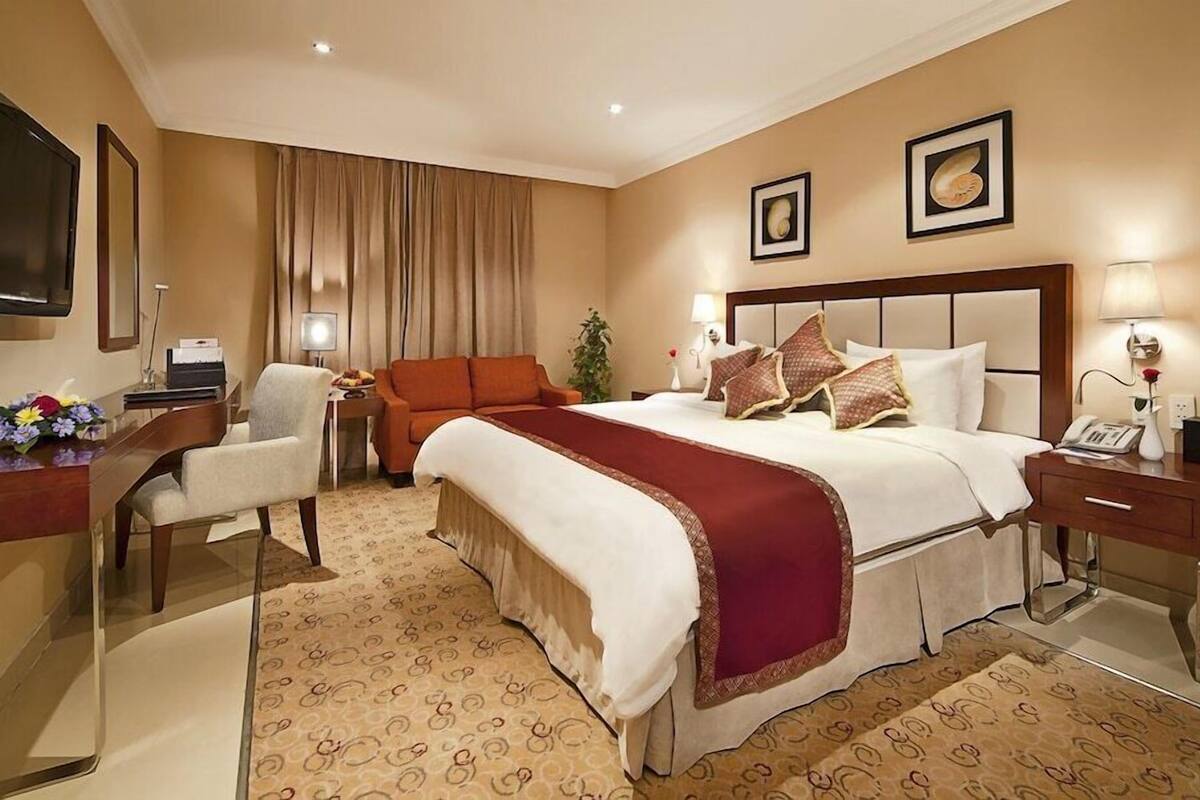 Ett hotellrum med en stor säng, ett skrivbord, en stol, en tv och en växt.