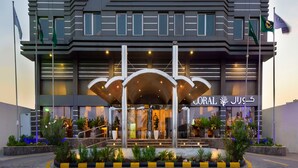 Una entrada de hotel moderna con vestíbulo cubierto, varias banderas y jardines bien cuidados.