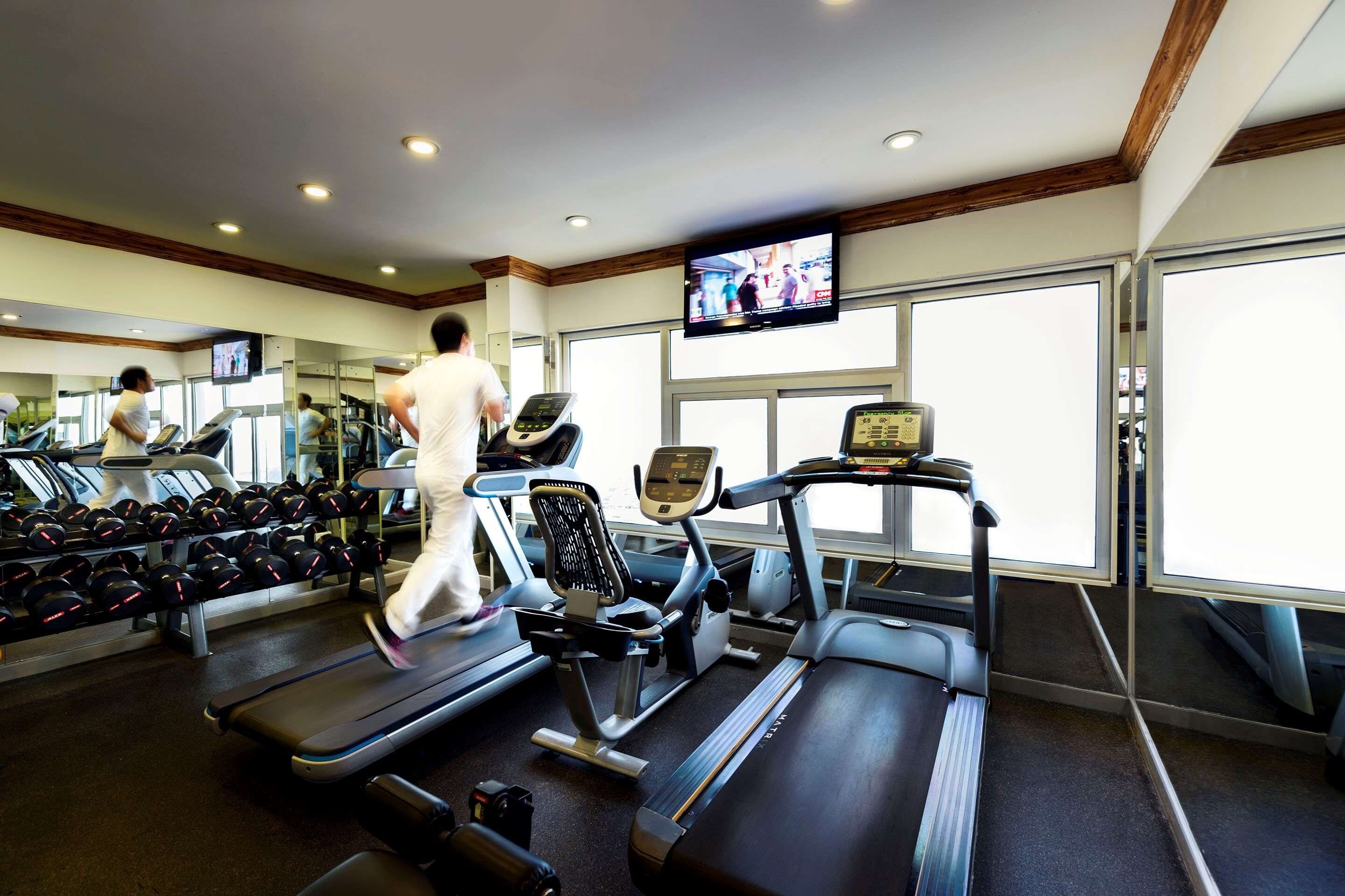 A gym with treadmills, dumbbells, and a TV screen.