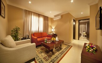 Una sala de estar moderna con un sofá color beige, un sillón rojo, una mesa de centro con bebidas y un jarrón decorativo.