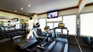 Un gimnasio con cintas de correr, mancuernas y una pantalla de televisión.