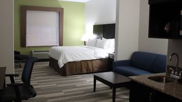 Habitación de hotel con cama, escritorio, silla, sofá y una zona de cocina con fregadero.