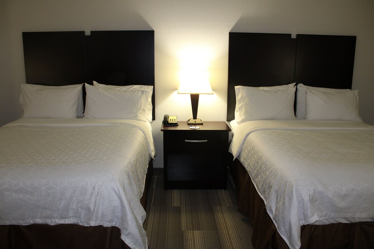 A hotel room with two beds, a nightstand with a lamp, and a telephone.