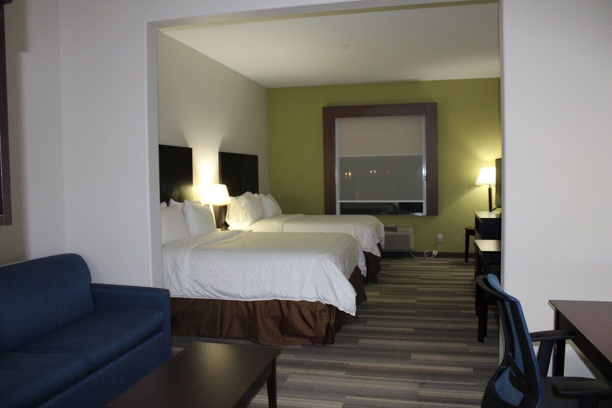 A hotel room with two beds, a desk, a chair, and a couch.