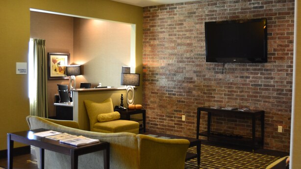 A hotel room with a yellow armchair, a sofa, a small table, a TV mounted on a brick wall, and a desk with a lamp. - Holiday Inn Express Heber Springs by IHG (Heber Springs)
