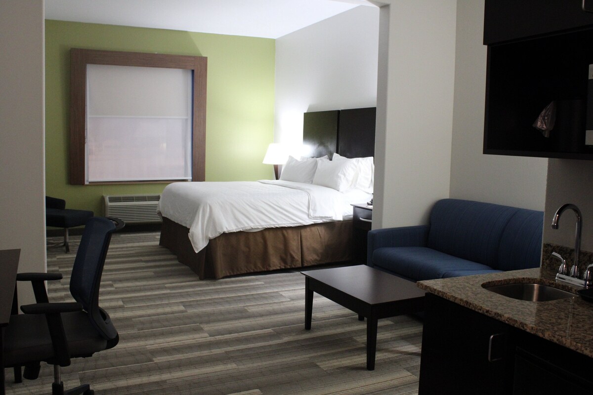 A hotel room with a bed, a desk, a chair, a sofa, and a bathroom area.