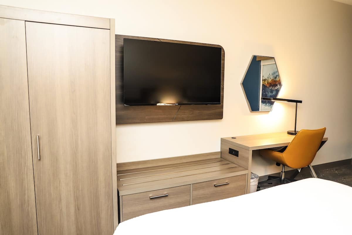 A hotel room with a bed, a desk with a chair, a wardrobe, a flat-screen TV, and a mirror.