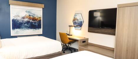 A hotel room with two beds, a desk with a chair, a TV, and artwork on the walls.