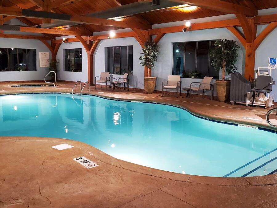 A swimming pool with a wooden deck, lounge chairs, and a spa area.