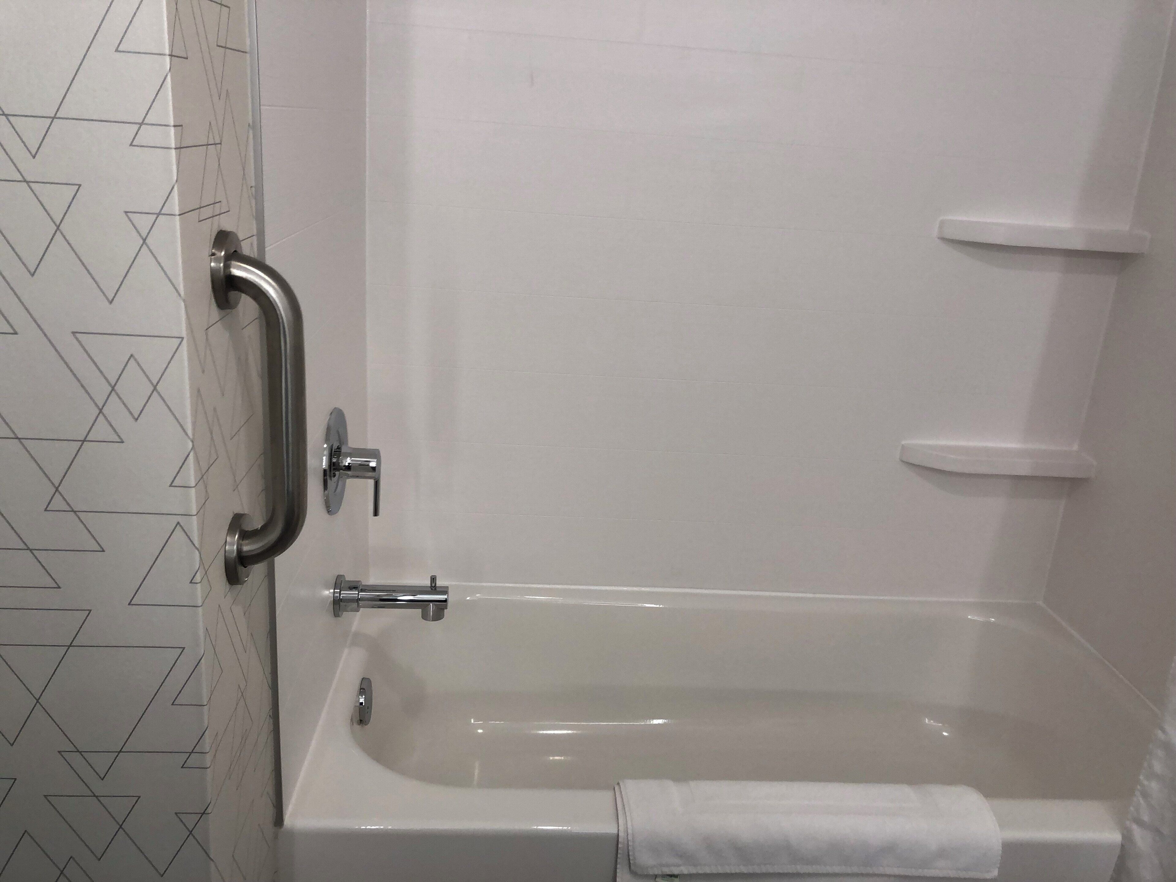 A bathroom with a bathtub, a handrail, and a towel.