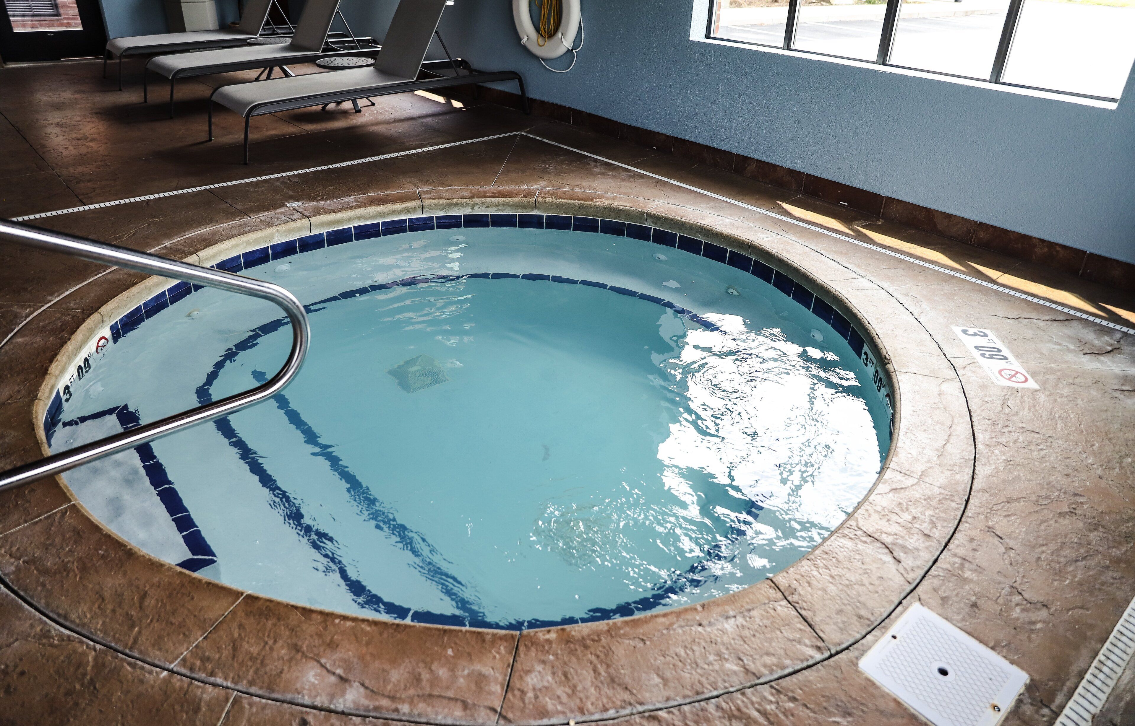 An indoor swimming pool with a tiled edge, a metal ladder, and lounge chairs.
