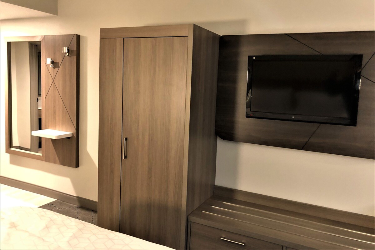 A modern room with a wardrobe, a mirror, and a flat-screen TV mounted on the wall.