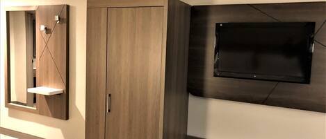 A room with a wardrobe, a mirror, a flat-screen TV mounted on the wall, and a marble-topped table.