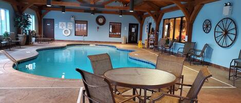 Una piscina interior con techo y paredes de madera, rodeada de sillas y mesas de mimbre.