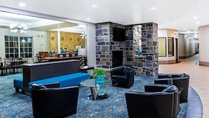 A lobby with a stone fireplace, blue sofa, black leather chairs, and a glass coffee table. - La Quinta Inn & Suites by Wyndham Denver Gateway Park (Denver)