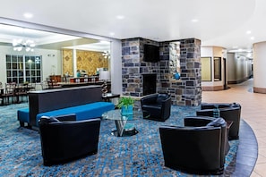 Un hall d’entrée avec une cheminée en pierre, un canapé bleu, des fauteuils en cuir noir et une table basse en verre.