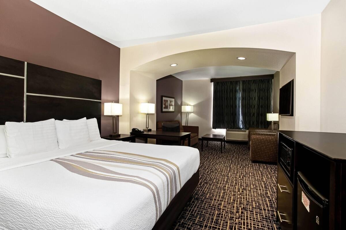 Ein Hotelzimmer mit einem großen Bett, einem Schreibtisch, zwei Stühlen, einem Fernseher und einem Spiegel.
