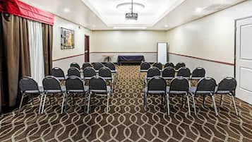 Un salón de conferencias con alfombra estampada, filas de sillas, un proyector y una pizarra.