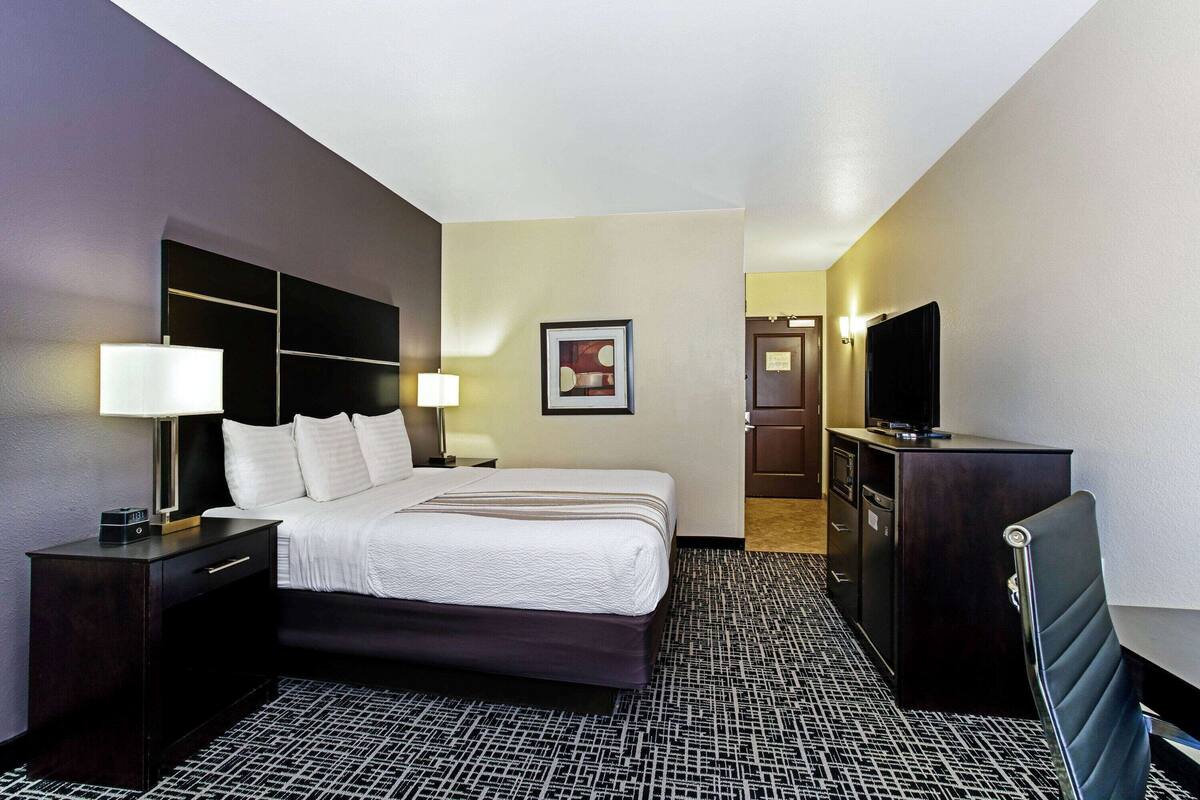 Ein Hotelzimmer mit Bett, Nachttischen, Schreibtisch, Stuhl, Fernseher und einem gerahmten Bild an der Wand.