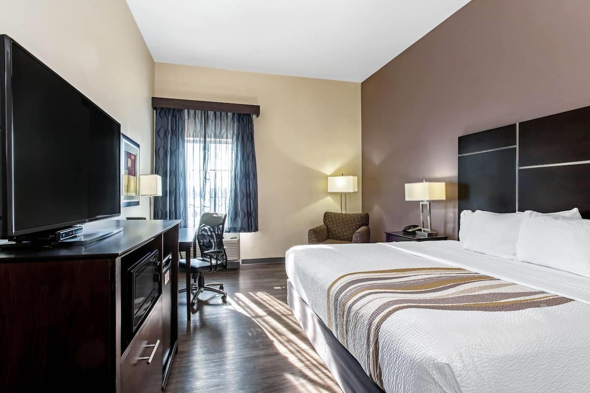 Ein Hotelzimmer mit einem Bett, einem Schreibtisch mit Fernseher, einem Sessel und einer Lampe.
