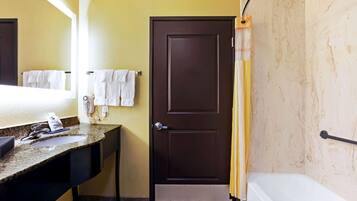 A bathroom with a sink, mirror, towel rack, door, and bathtub.