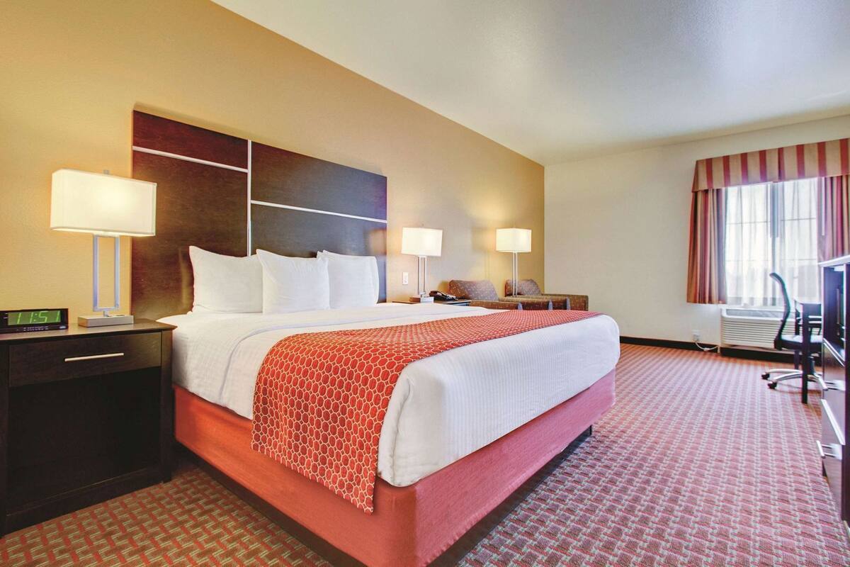 Ein Hotelzimmer mit einem großen Bett, Nachttischlampen, einem Schreibtisch, einem Stuhl und einem Fenster mit Vorhängen.