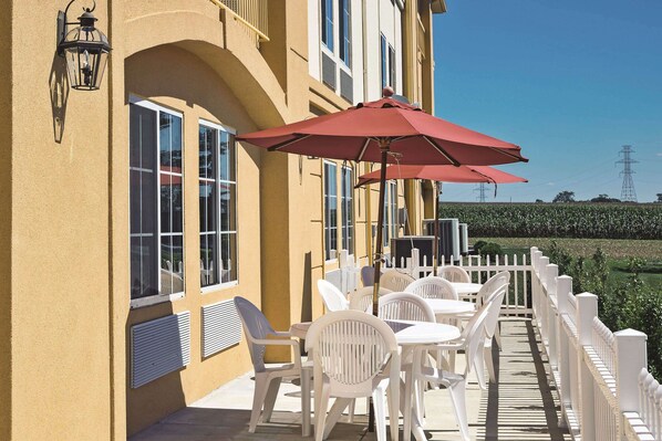 Une terrasse avec des chaises et des tables en plastique blanc, un parasol rouge et une clôture en bois peinte en blanc.
