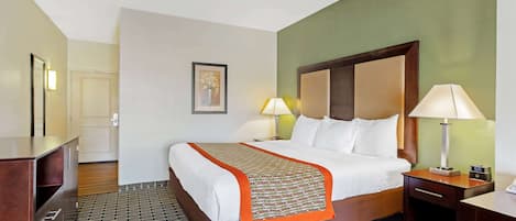 Une chambre d’hôtel avec un grand lit, deux tables de chevet avec des lampes, une tête de lit en bois, un tableau encadré au mur et un sol à motifs.
