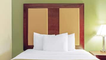 Habitación de hotel con una cama grande, paredes verdes, cabecera de madera y una mesita de noche con lámpara.