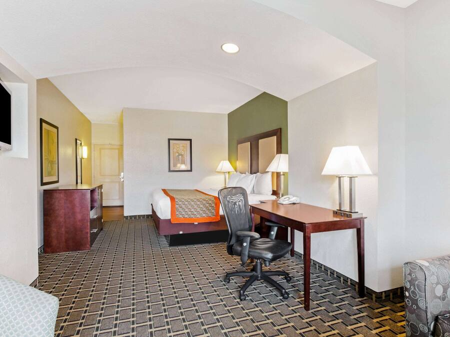 A hotel room with a bed, desk, chair, and two lamps.