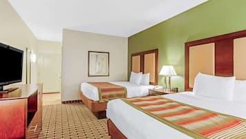 Quarto de hotel com duas camas, televisão, escrivaninha e tapete estampado.