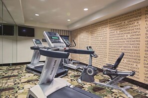Une salle de sport d’hôtel équipée de tapis de course, d’un vélo d’appartement et d’un banc de musculation.