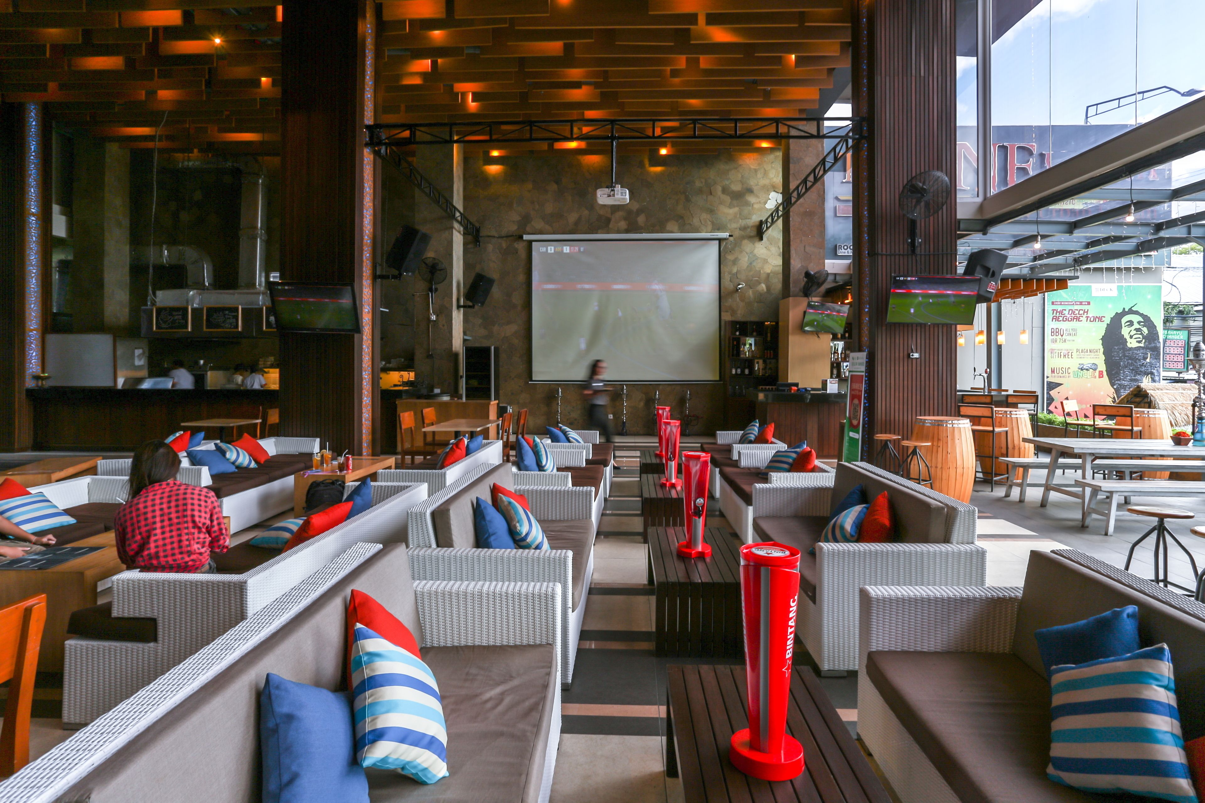 A modern outdoor seating area with wicker furniture and red accents, a projection screen, and a view of the cityscape.
