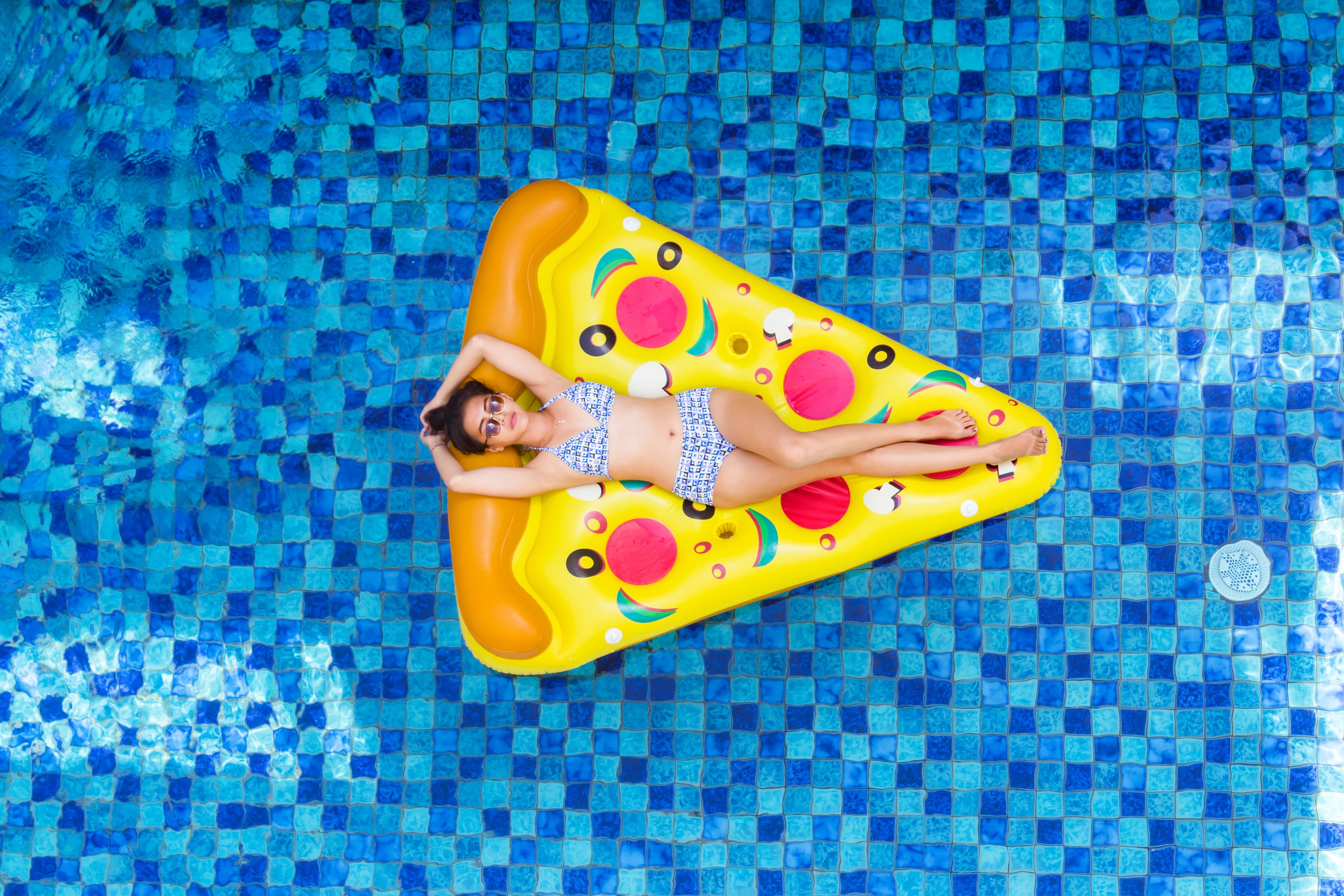 A person lying on a yellow inflatable pool float shaped like a pizza in a swimming pool.