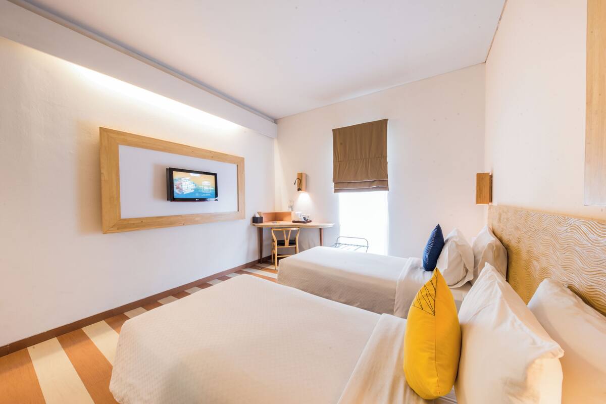 Una habitación de hotel con dos camas, un escritorio, un televisor y una ventana con persiana marrón.
