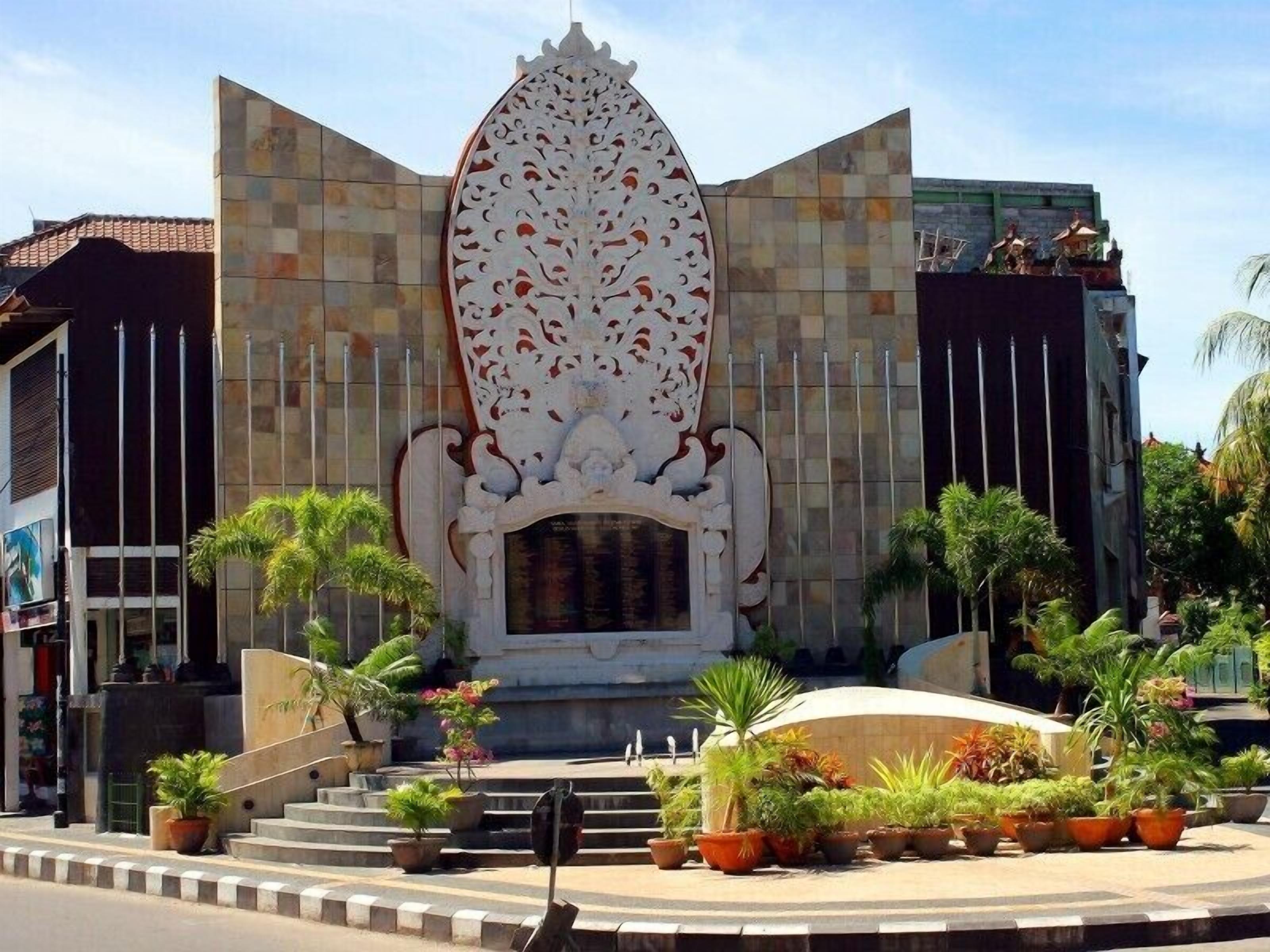 A building with a large decorative archway and steps leading up to it, surrounded by potted plants.
