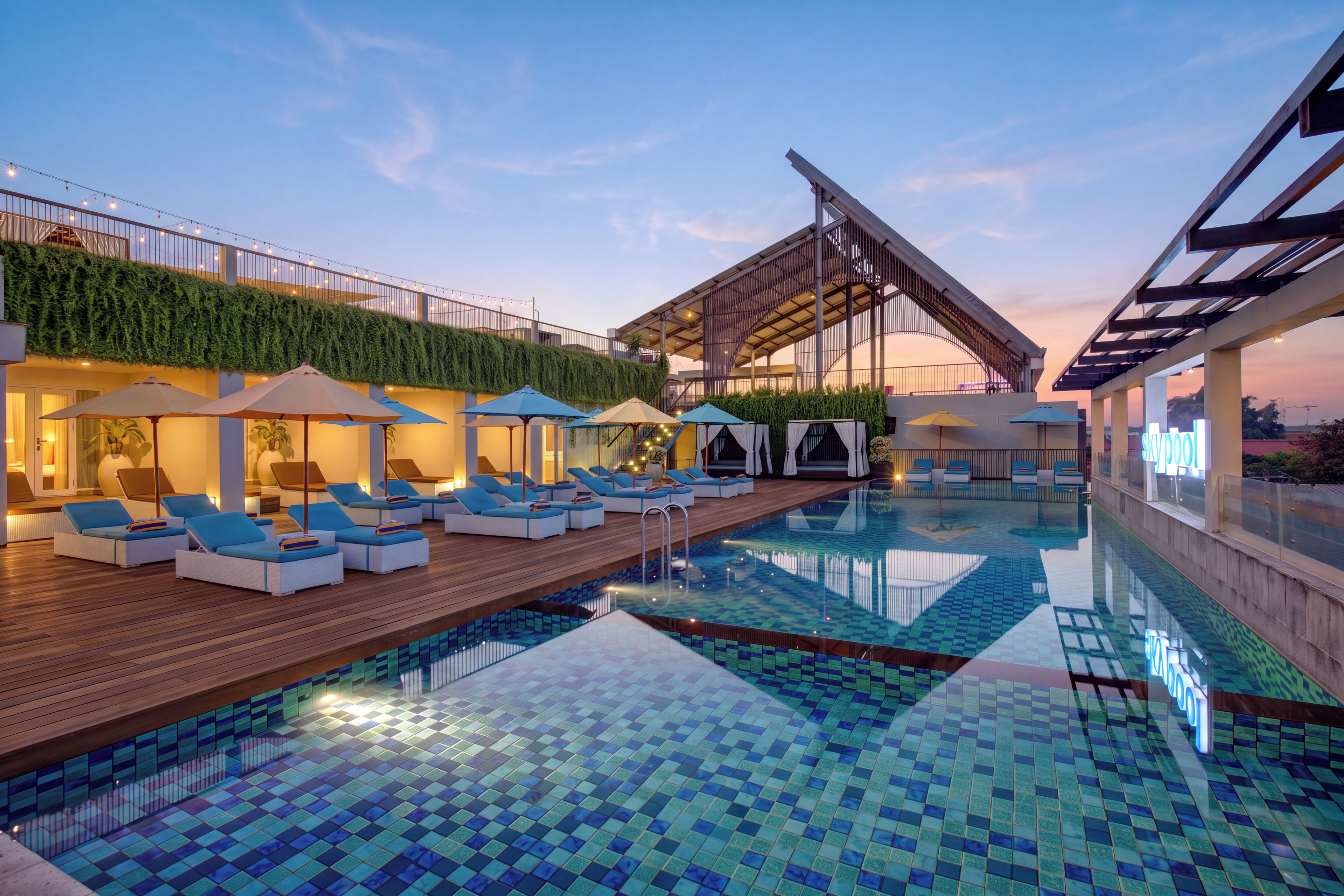 A swimming pool with lounge chairs and umbrellas, surrounded by a building with a green wall and a covered area.