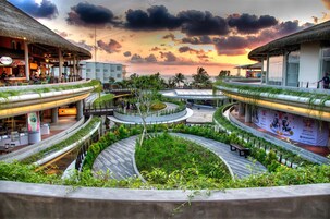 Un resort con un paseo central circular rodeado de exuberante vegetación, varias zonas de comedor y vistas al atardecer.