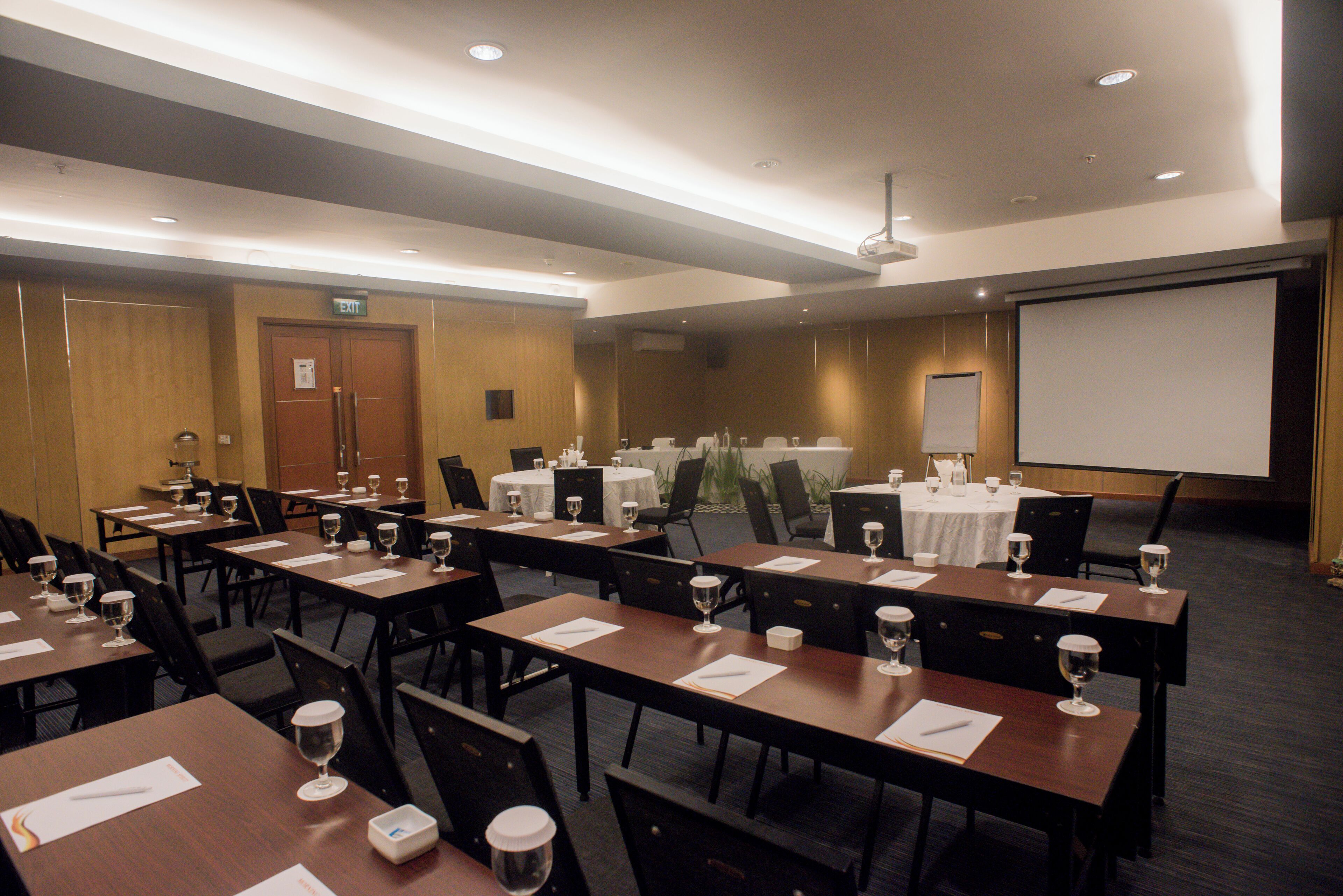 A conference room with multiple tables, chairs, and a projector screen.
