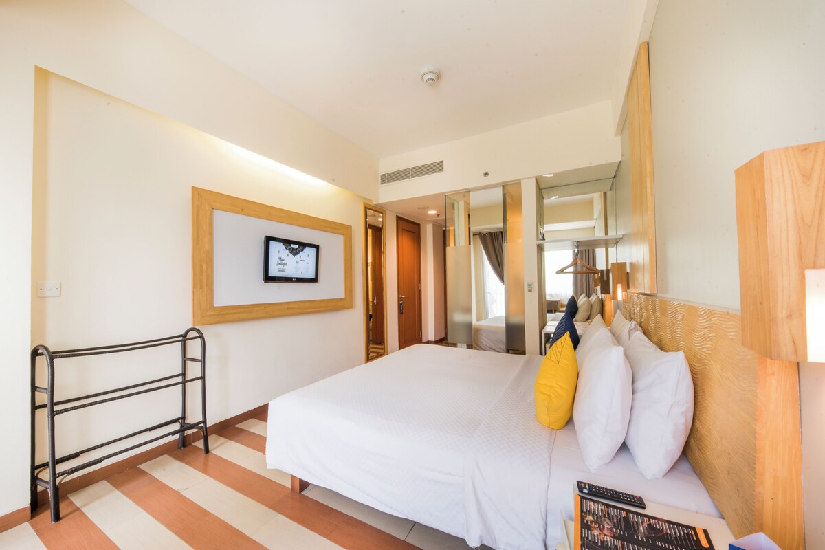 A hotel room with a large bed, a bedside table, a mirror, and a framed picture on the wall.