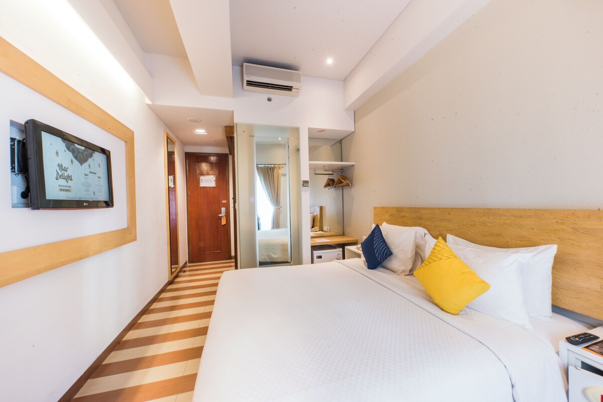 A hotel room with a large bed, a television mounted on the wall, a wooden headboard, and a striped floor.